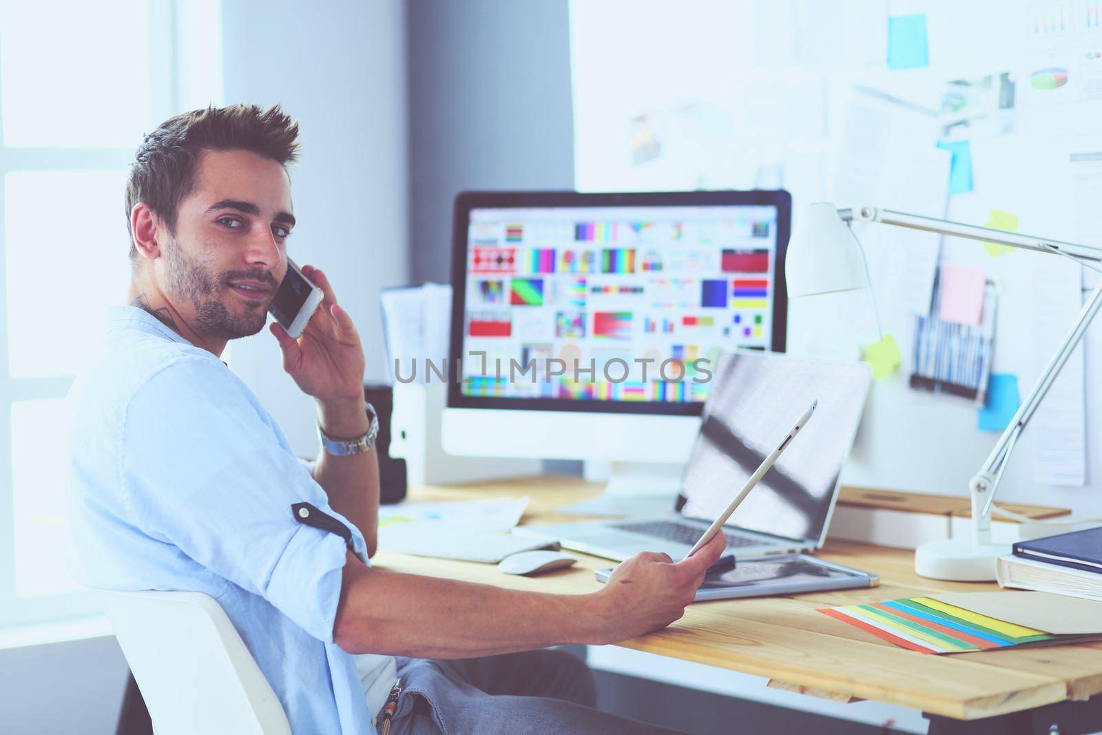 Portrait of young designer sitting at graphic studio in front of laptop and computer while working online