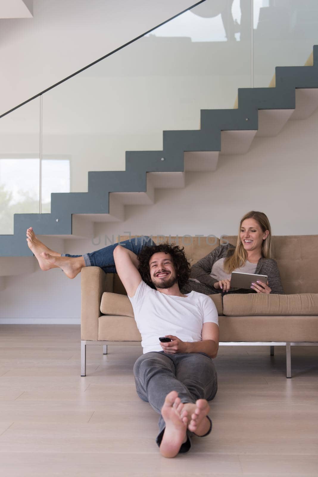 Young couple relaxes on the sofa in the luxury living room, using a tablet and remote control