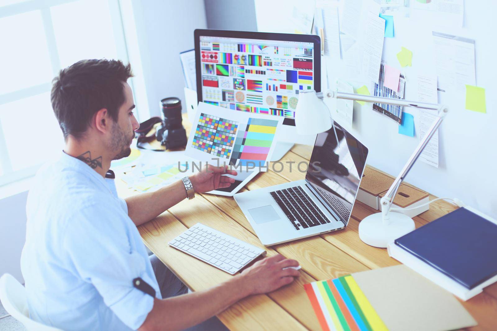 Portrait of young designer sitting at graphic studio in front of laptop and computer while working online