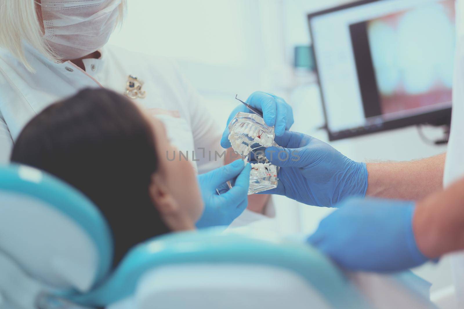 Senior male dentist in dental office talking with female patient and preparing for treatment by lenets