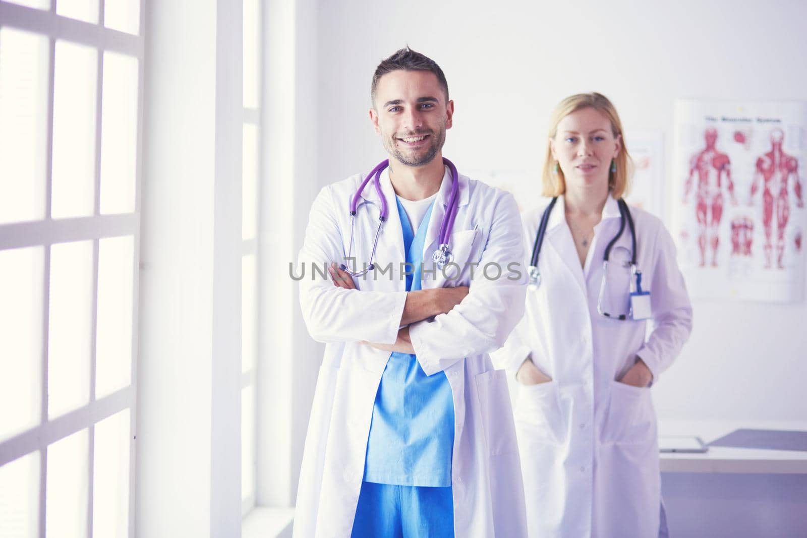 Handsome doctor is talking with young female doctor and making notes while sitting in his office