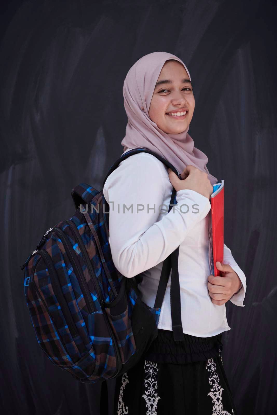 portrait of happy female middle eastern university student against black chalkboard in classroom