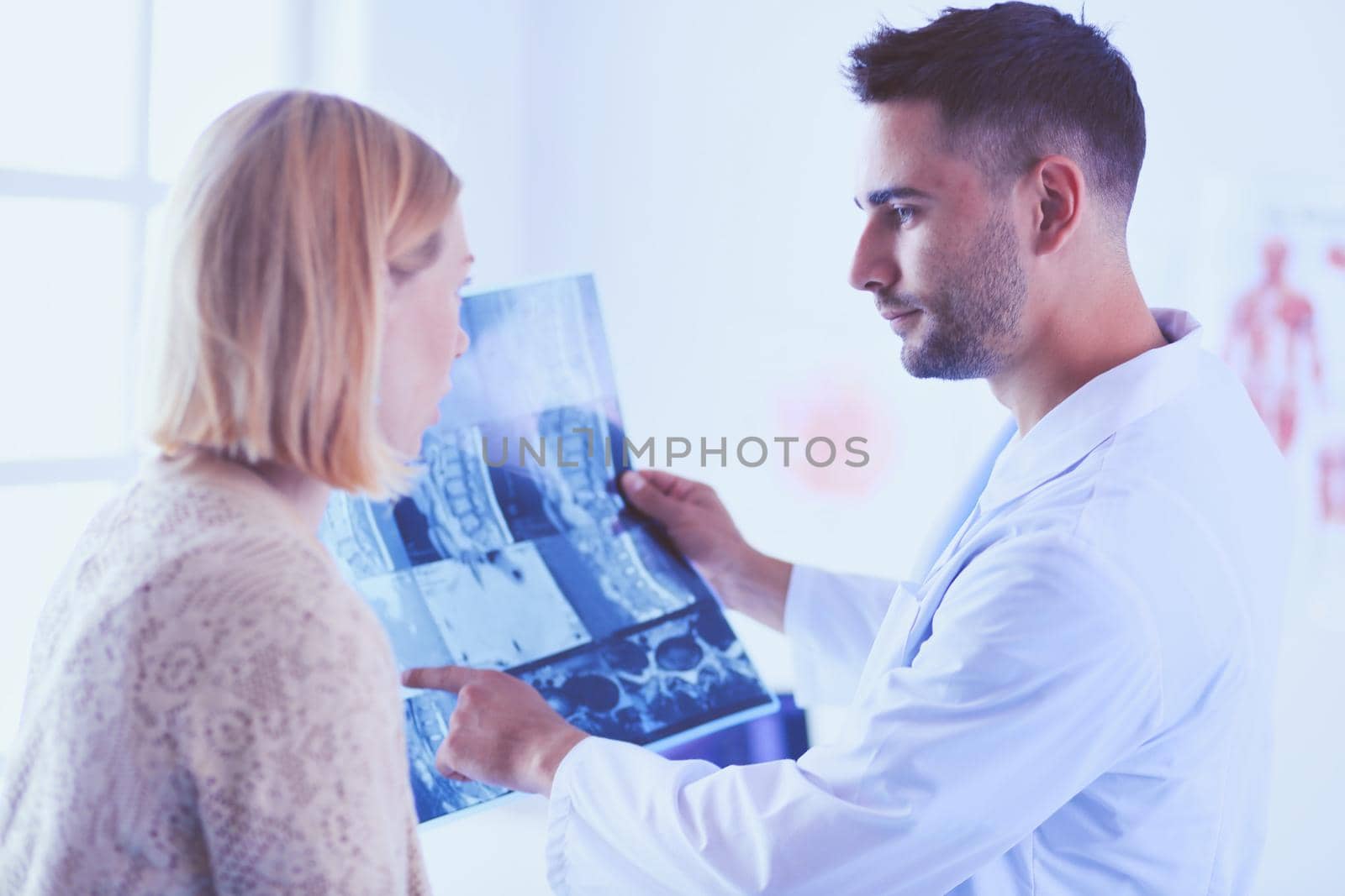 Handsome doctor is talking with young female patient and making notes while sitting in his office