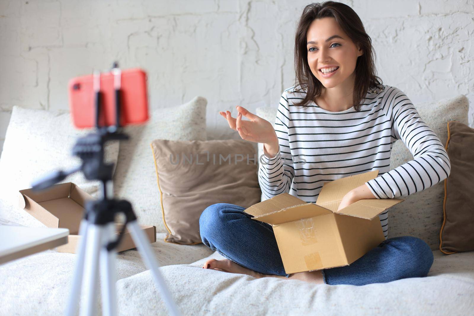 Young beautiful female blogger recording video while unpacking parcel at home. by tsyhun