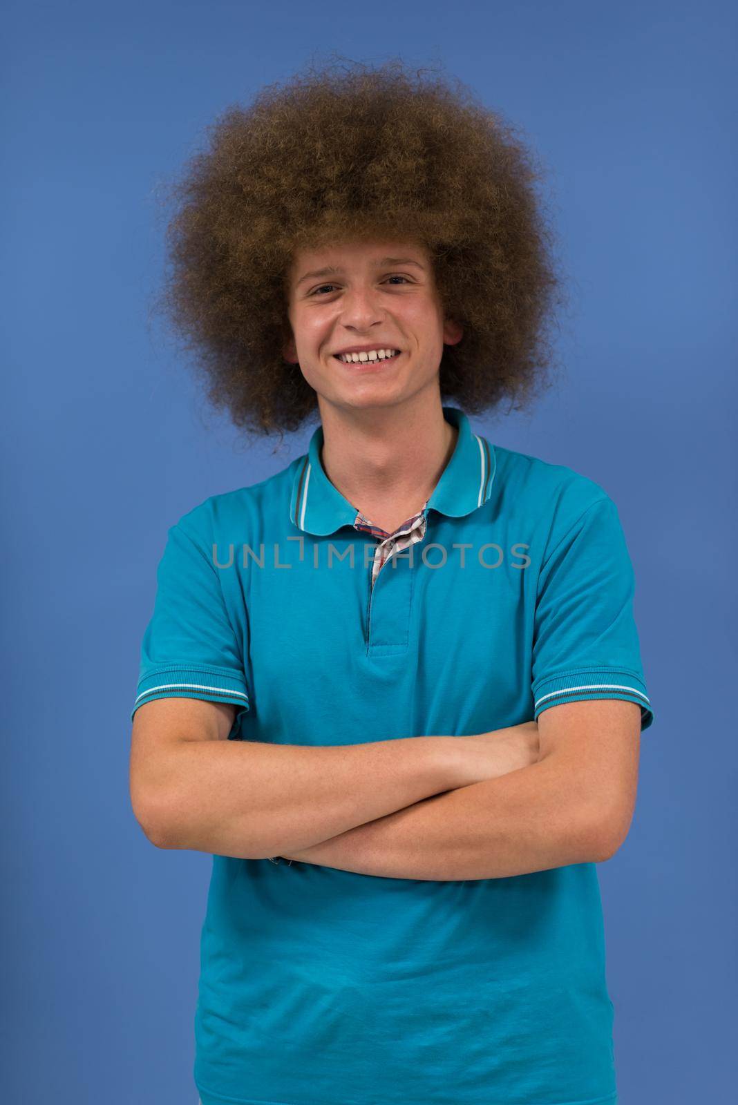 portrait of a young man with a funky hairstyle with arms crossed on blue background