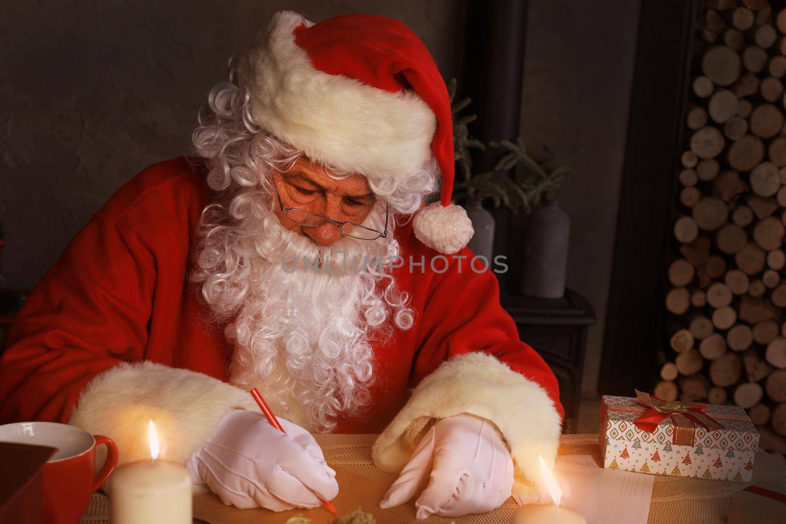 Portrait of happy Santa Claus sitting at his room at home near Christmas tree and answering Christmas letters
