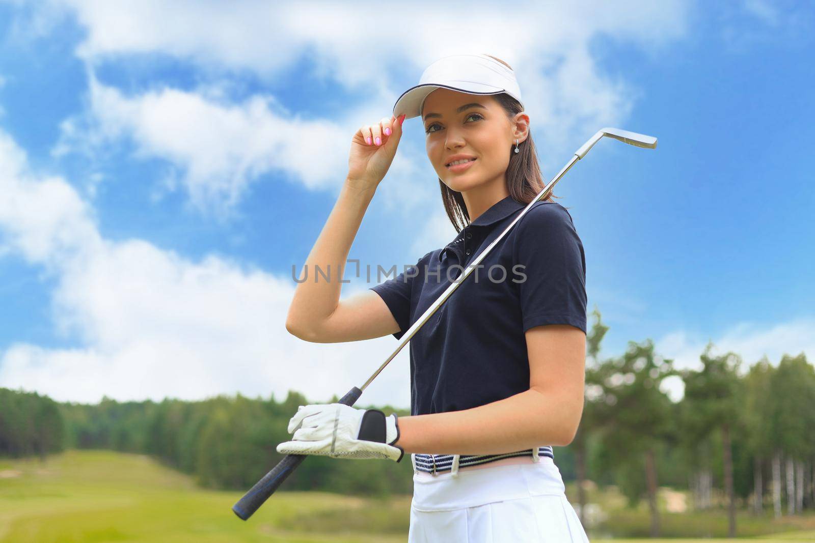Professional female golfer holding golf club on field and looking away. Young woman standing on golf course on a sunny day.