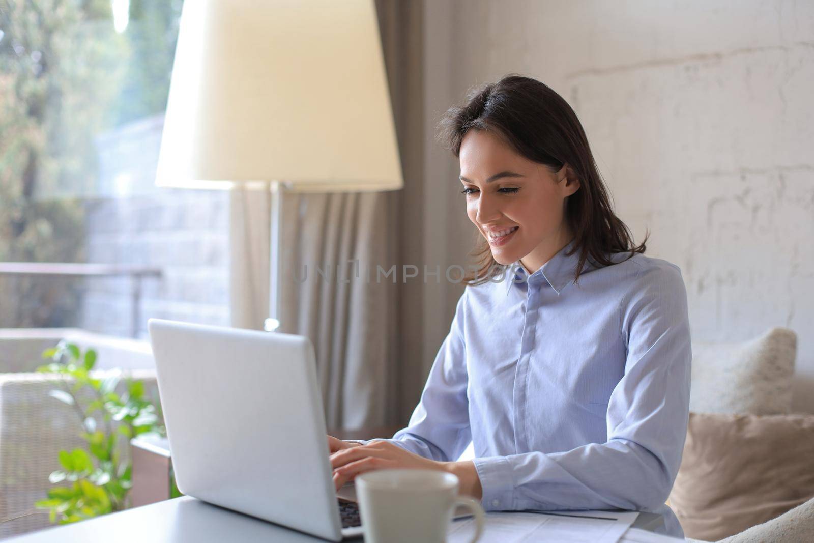 Smiling pretty woman sitting at table, looking at laptop screen. Happy entrepreneur reading message email with good news, chatting with clients online
