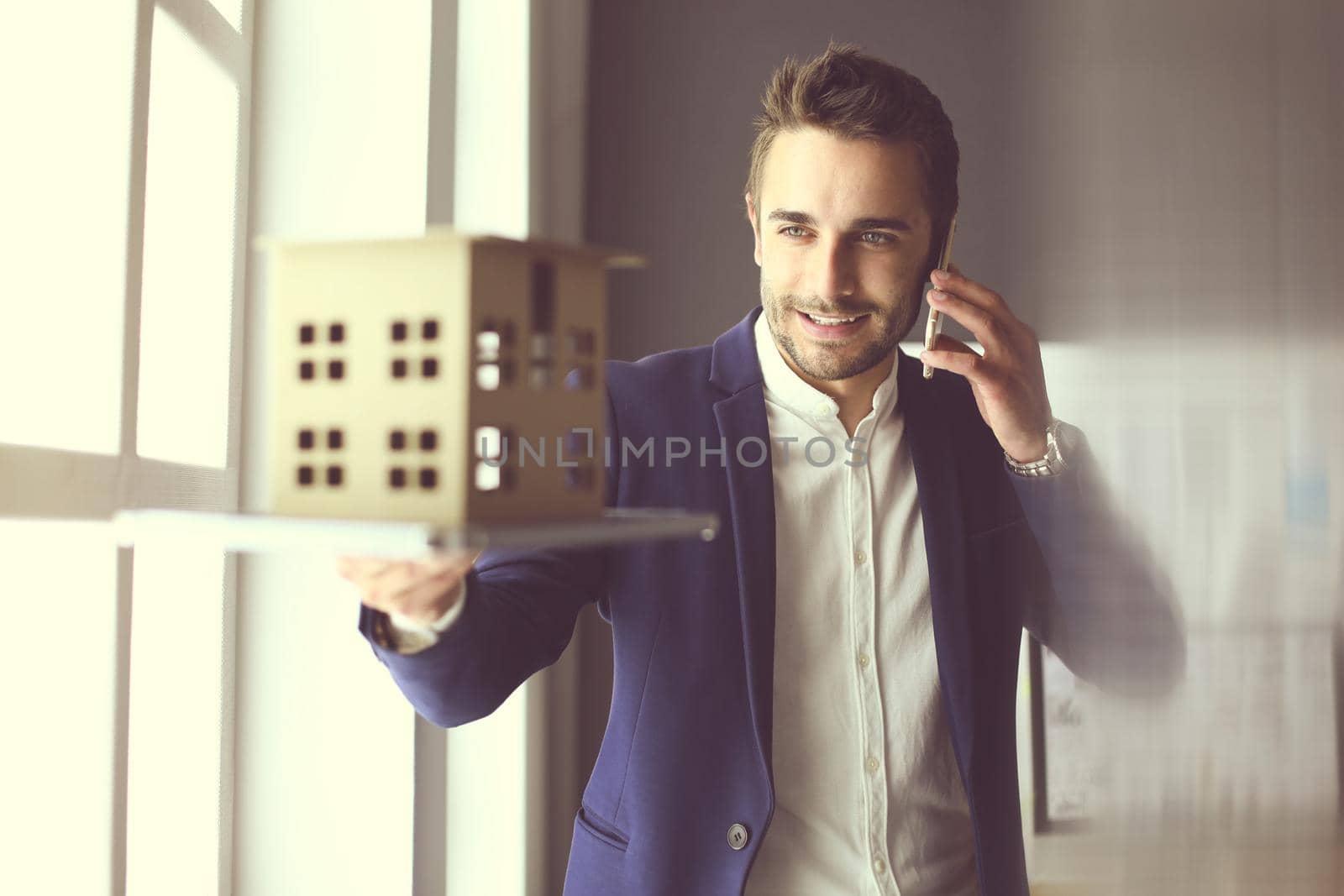 Businessman holding house miniature on hand standing in office