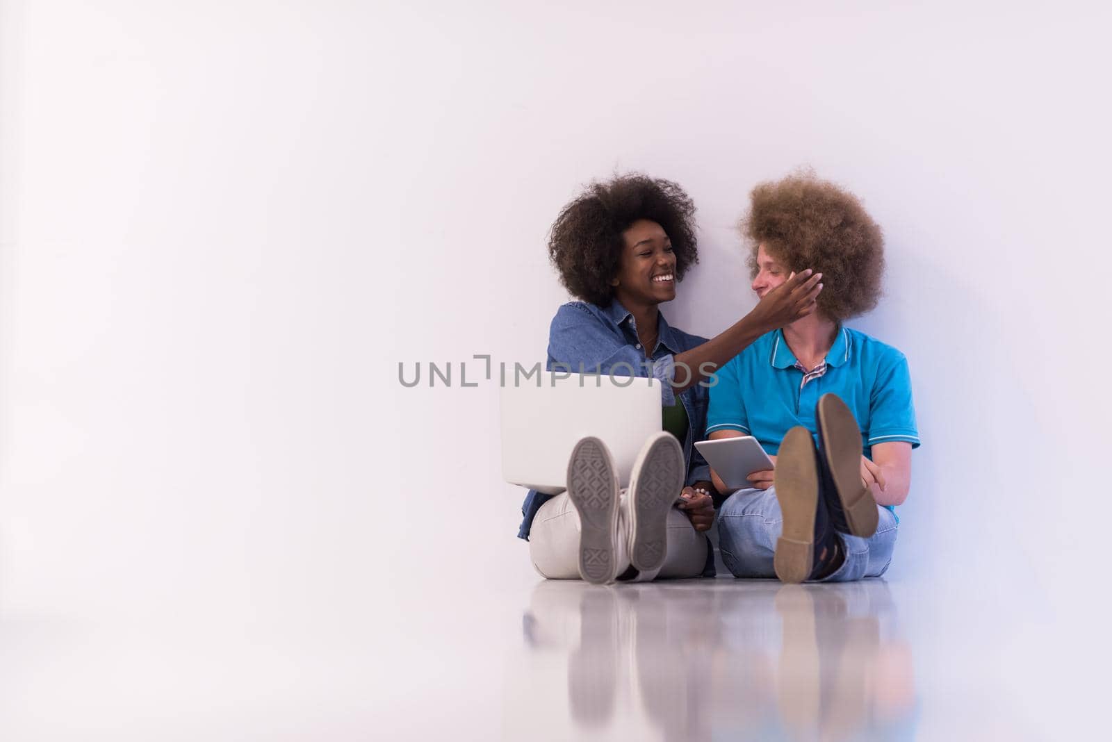 multiethnic couple sitting on the floor with a laptop and tablet by dotshock