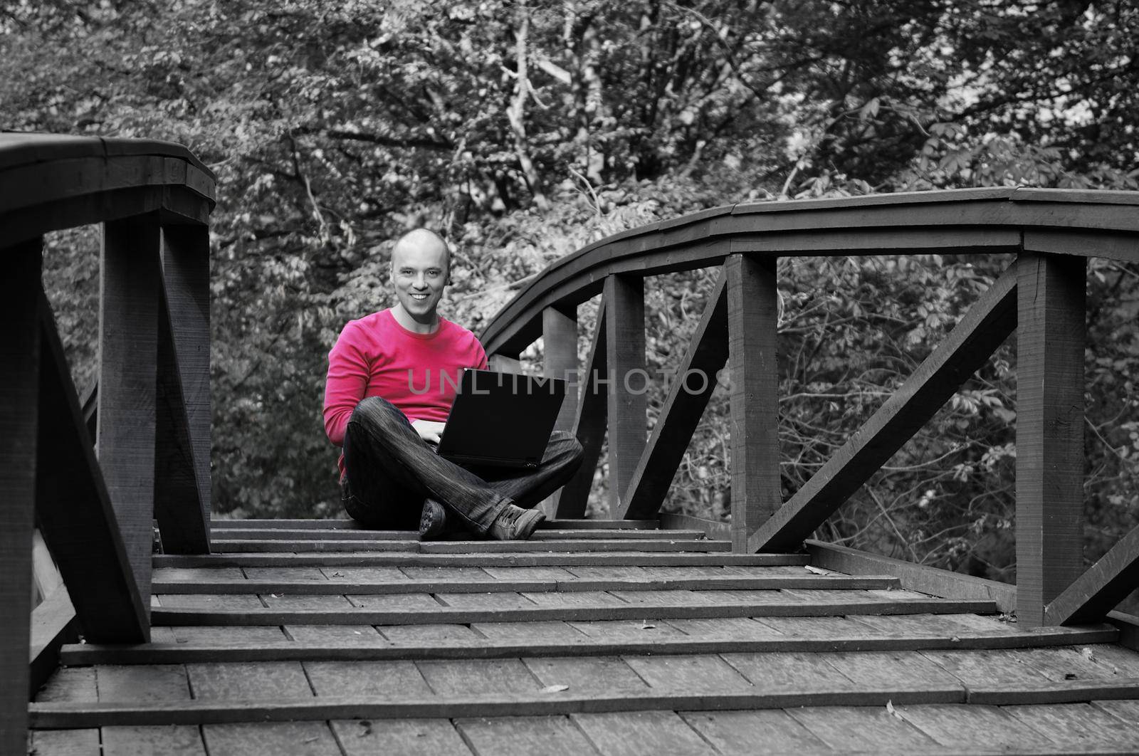 young sucessful businessman in red shirt working on laptop, outdoor on bridge