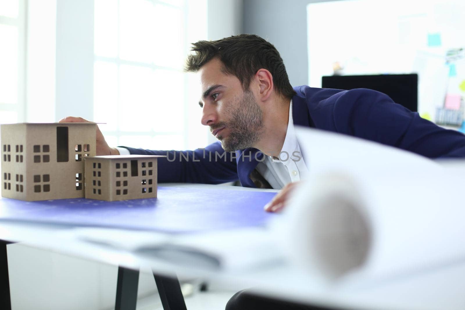 Businessman holding house miniature on hand standing in office