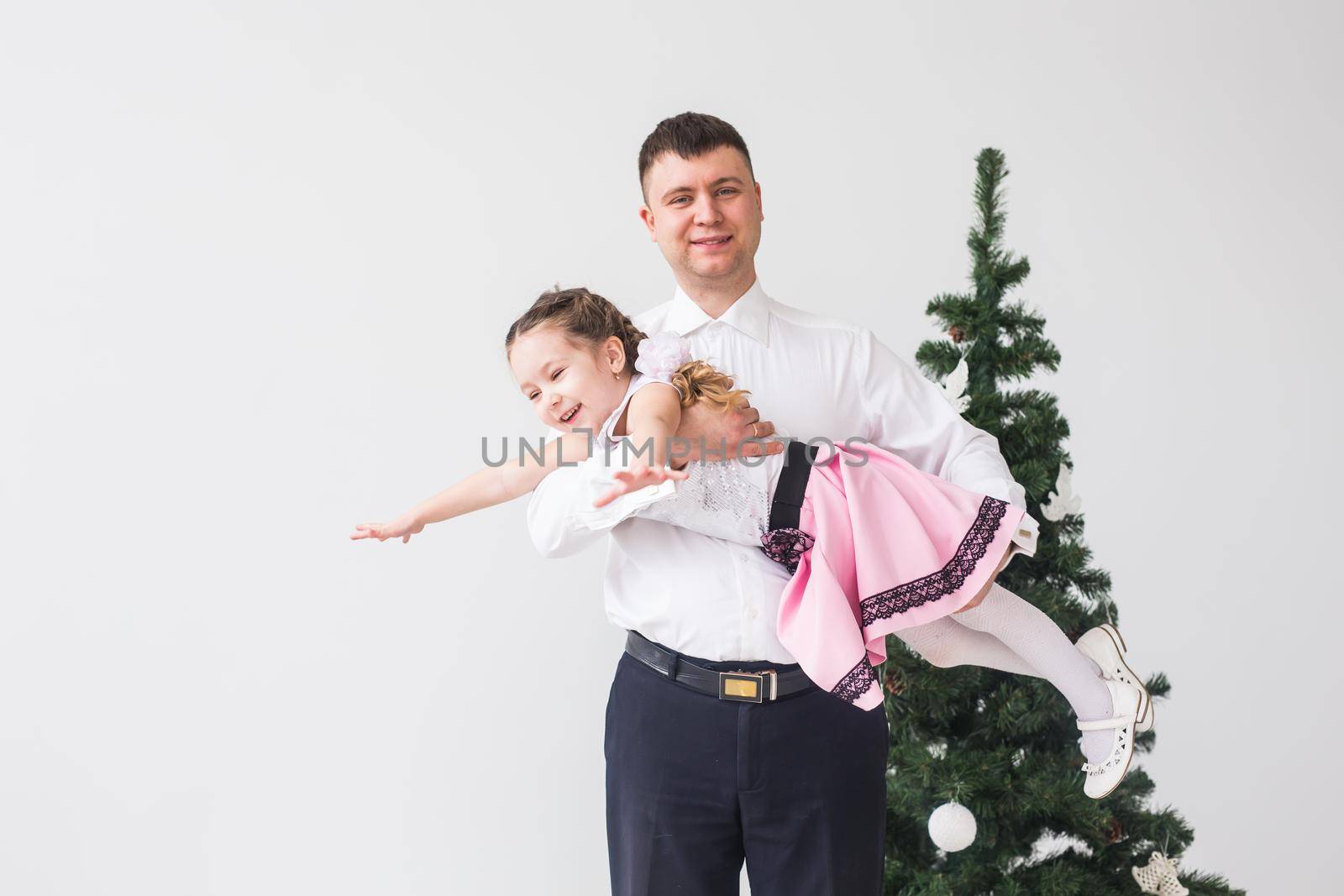 Children, festive and holidays concept - Father and daughter having fun near christmas tree.