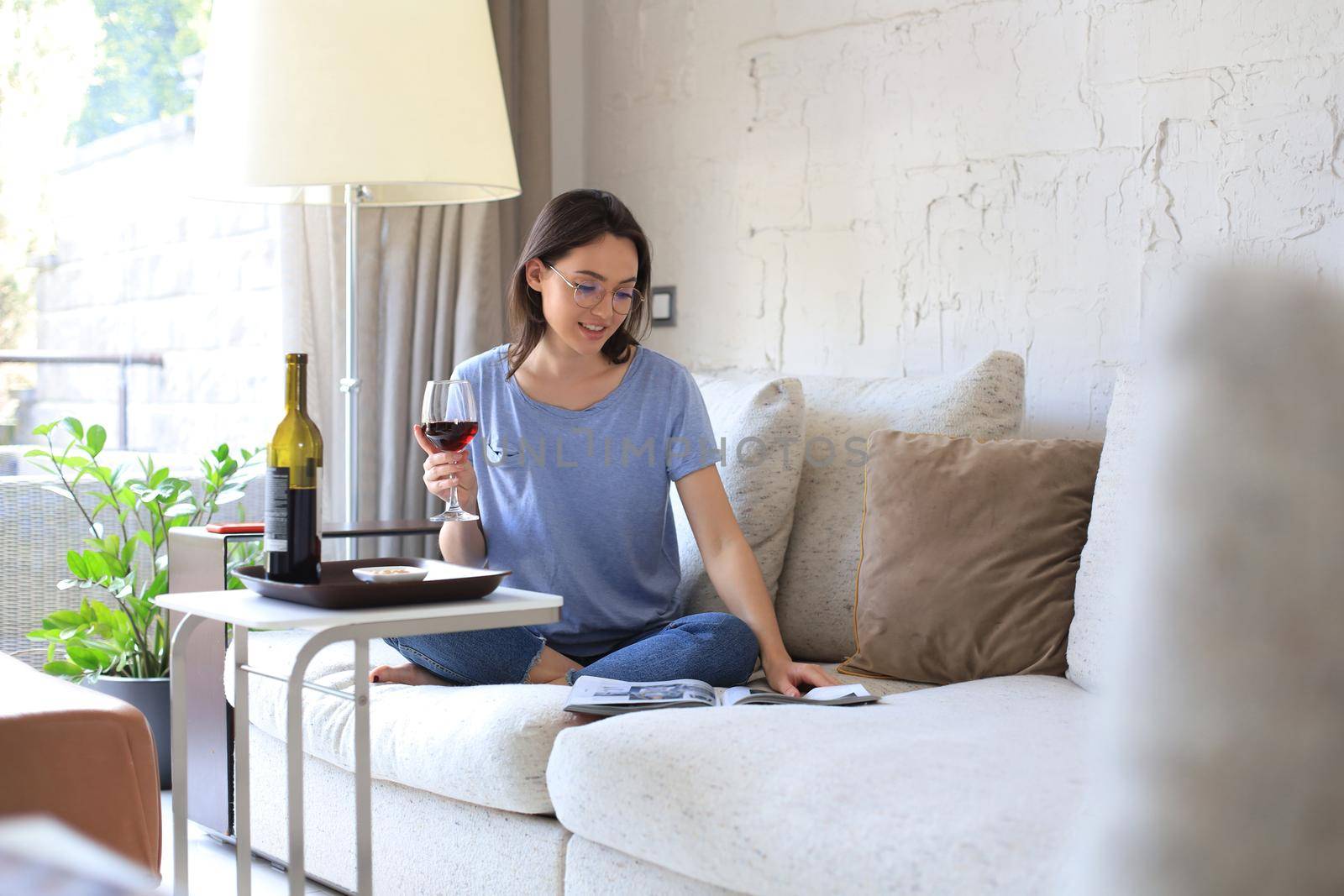 Successful young beautiful woman sitting on a sofa in the living room, drinking red wine