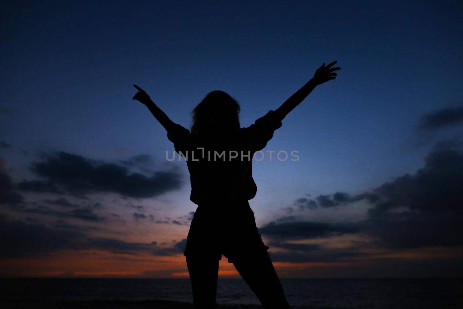 Silhouette of woman in sunset dark blue sky with clouds background. by sisterspro