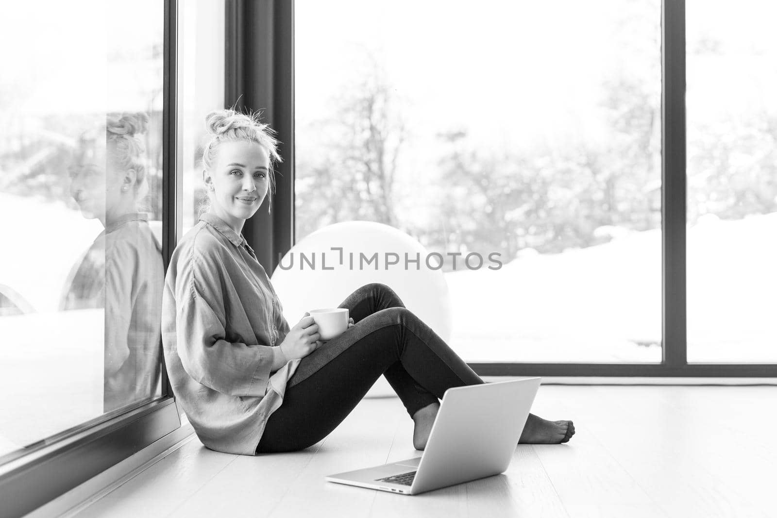 woman drinking coffee and using laptop at home by dotshock