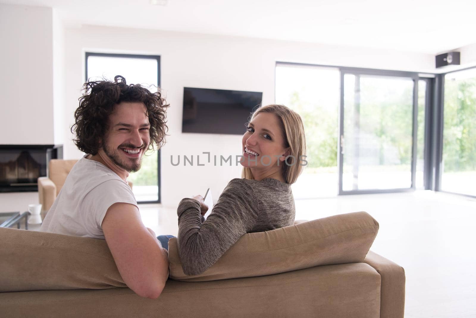 Rear view of couple watching television in living room their luxury home
