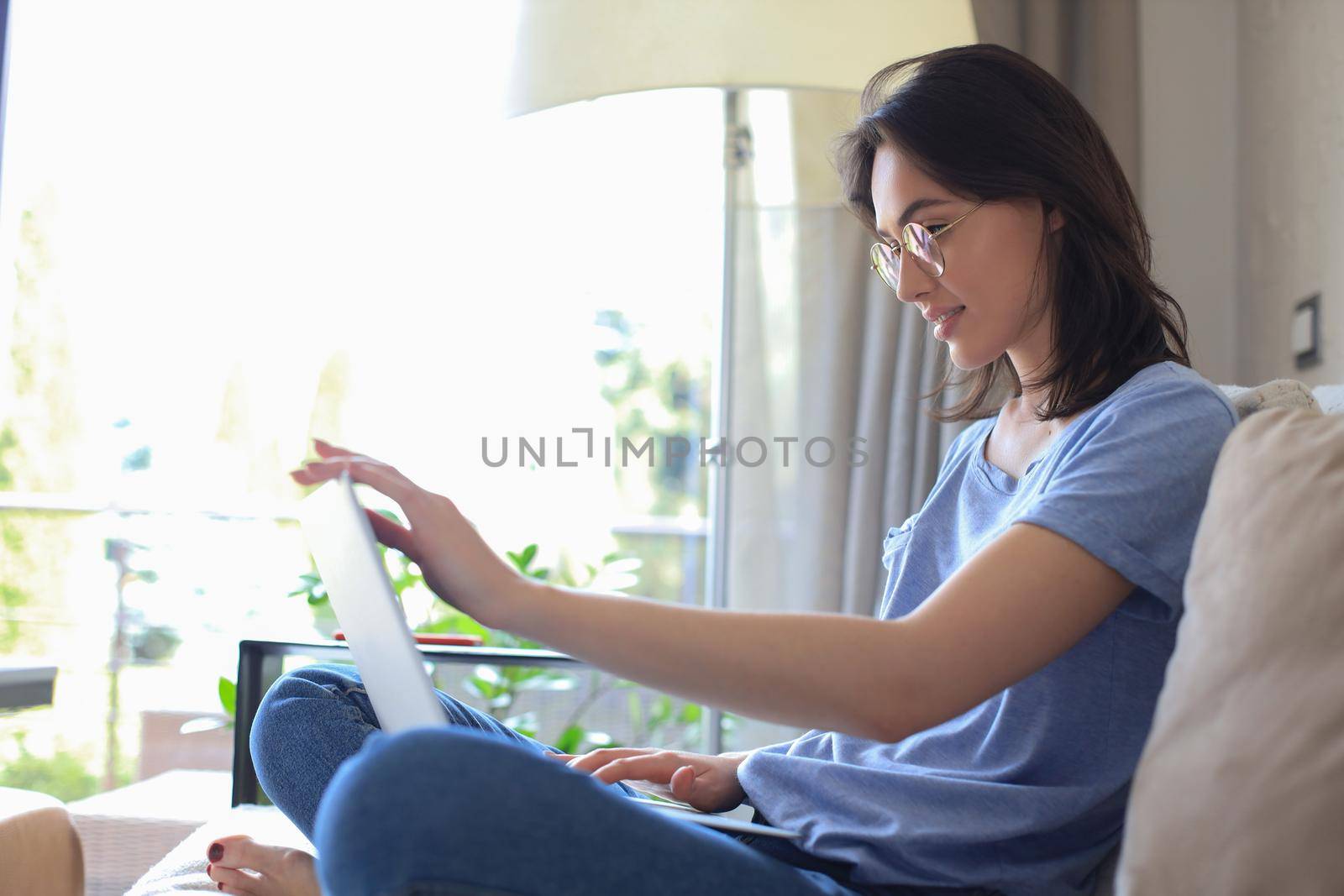 Smiling young woman sitting on sofa with laptop computer and chating with friends