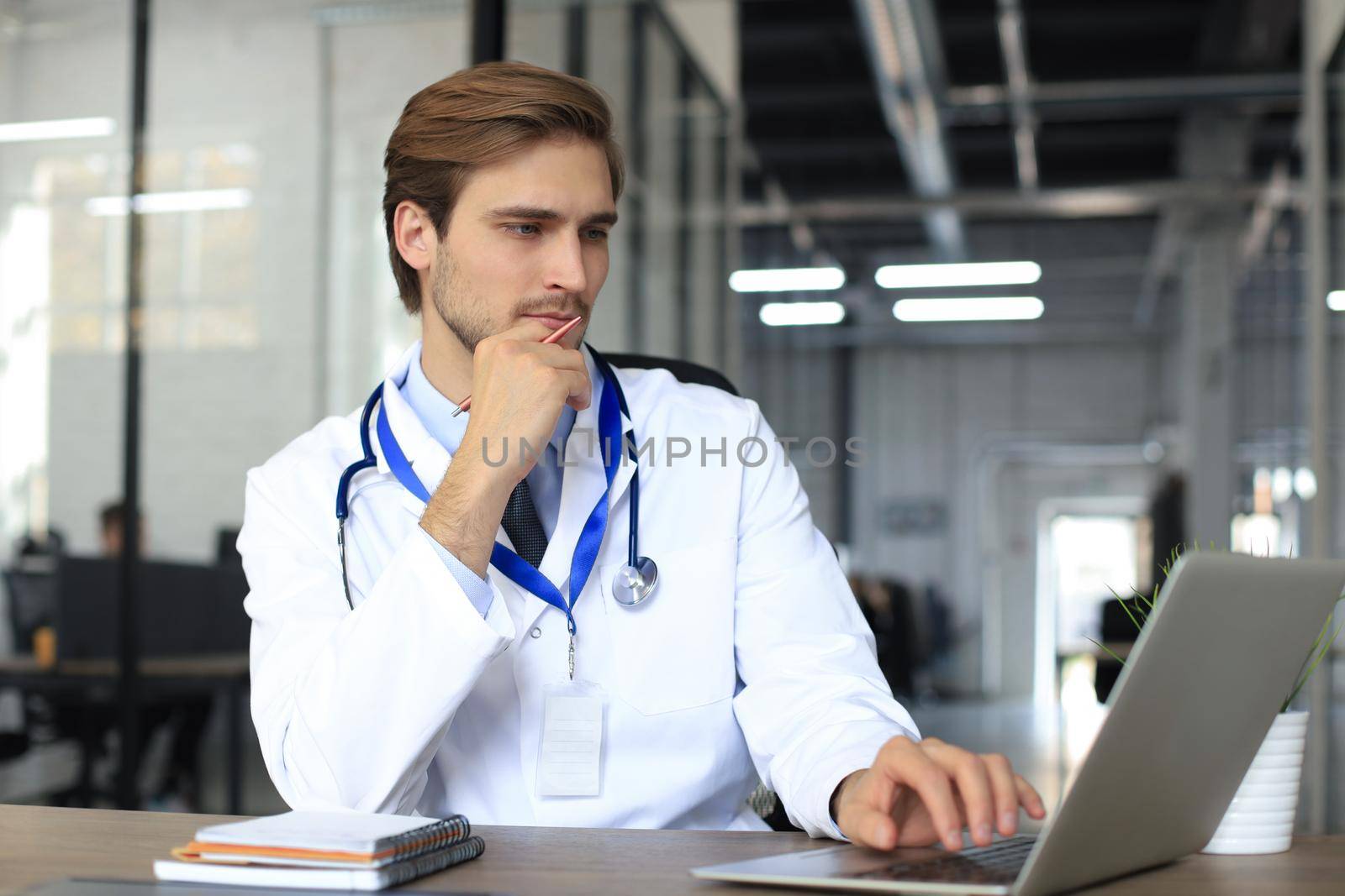 Doctor in white medical uniform with statoscope reading personal file of patient on tablet and writes data to laptop