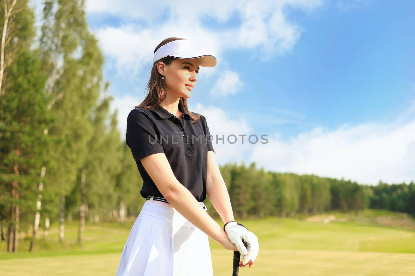 Professional female golfer holding golf club on field and looking away. Young woman standing on golf course on a sunny day.
