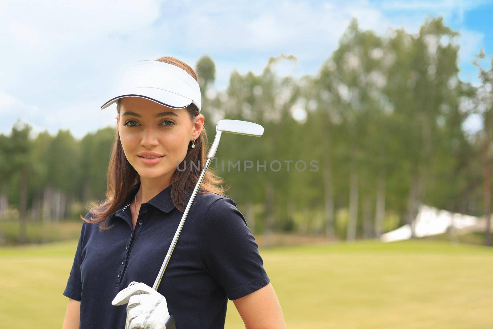 Professional female golfer holding golf club on field and looking away. Young woman standing on golf course on a sunny day.