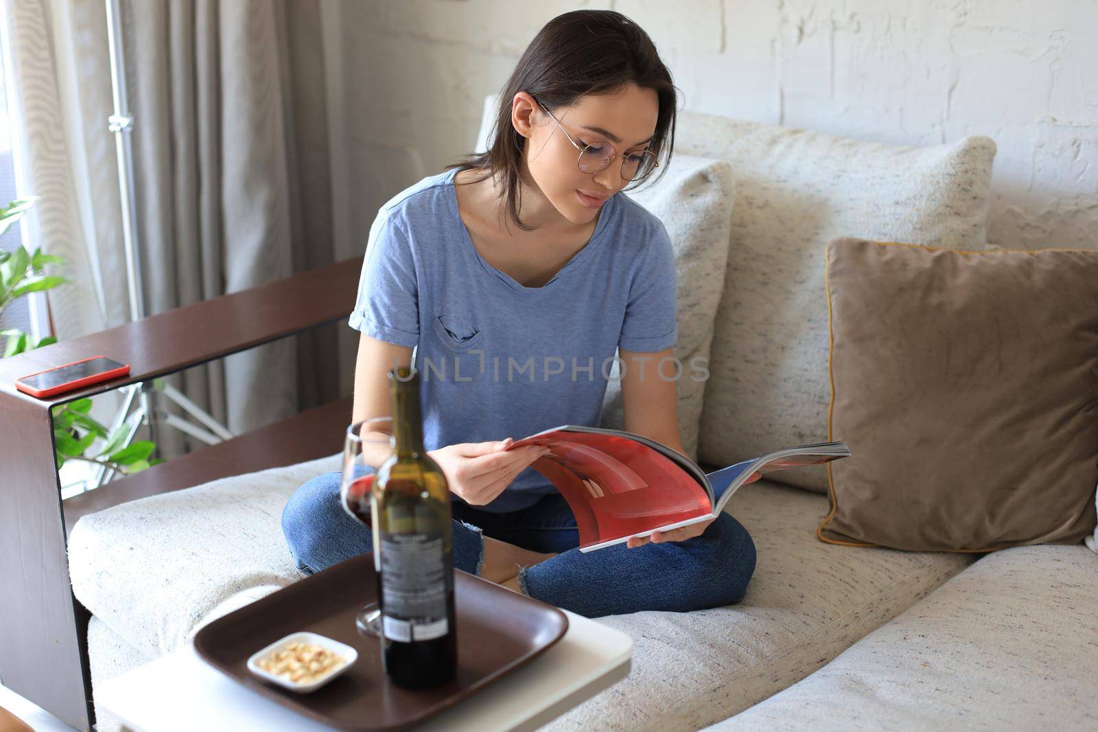 Successful young beautiful woman sitting on a sofa in the living room, drinking red wine