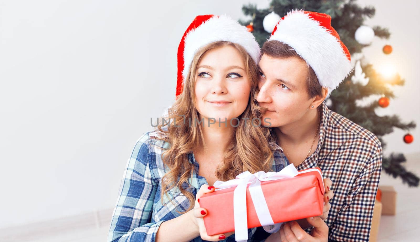 Family, x-mas, winter holidays and people concept - happy couple hugging near christmas tree at home.