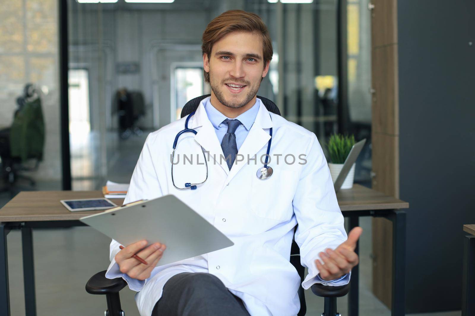 Smiling handsome male doctor talking at camera with patient