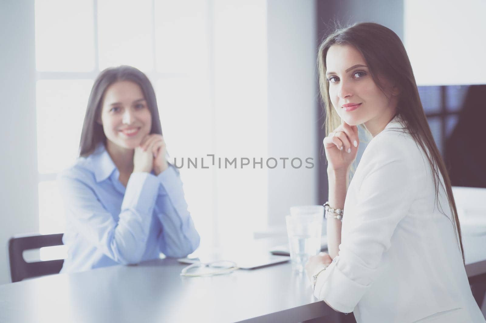 Two female colleagues in office sitting on the desk.