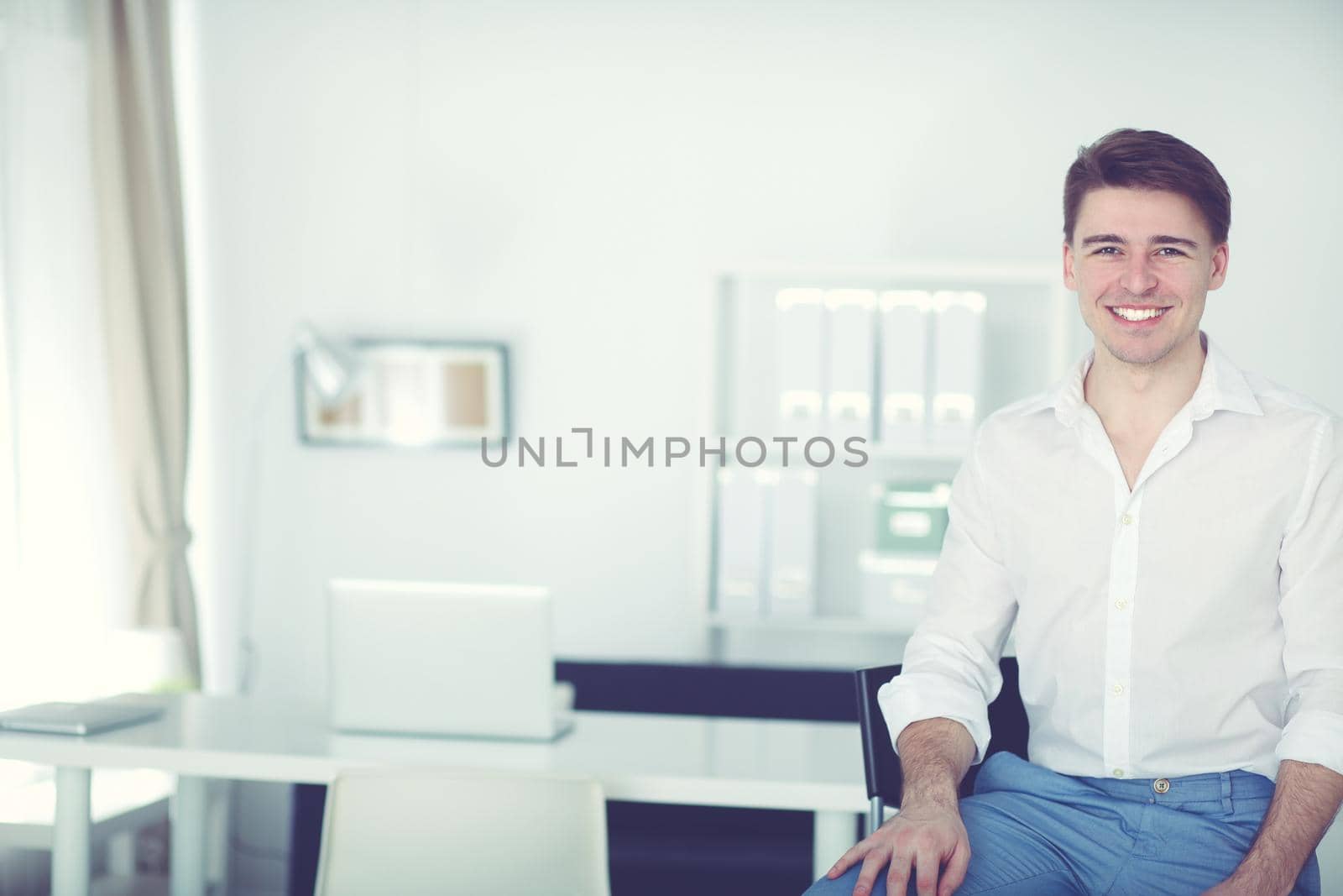 Happy young business man sitting at desk in office.