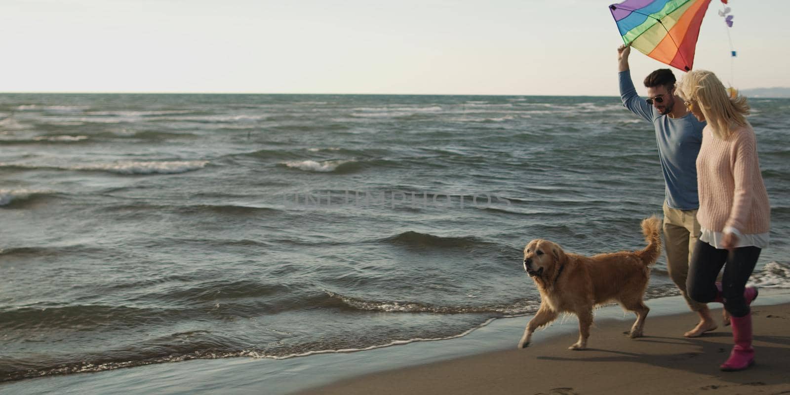 Couple Running On The Beach Holding Their Hands with dog On autmun day