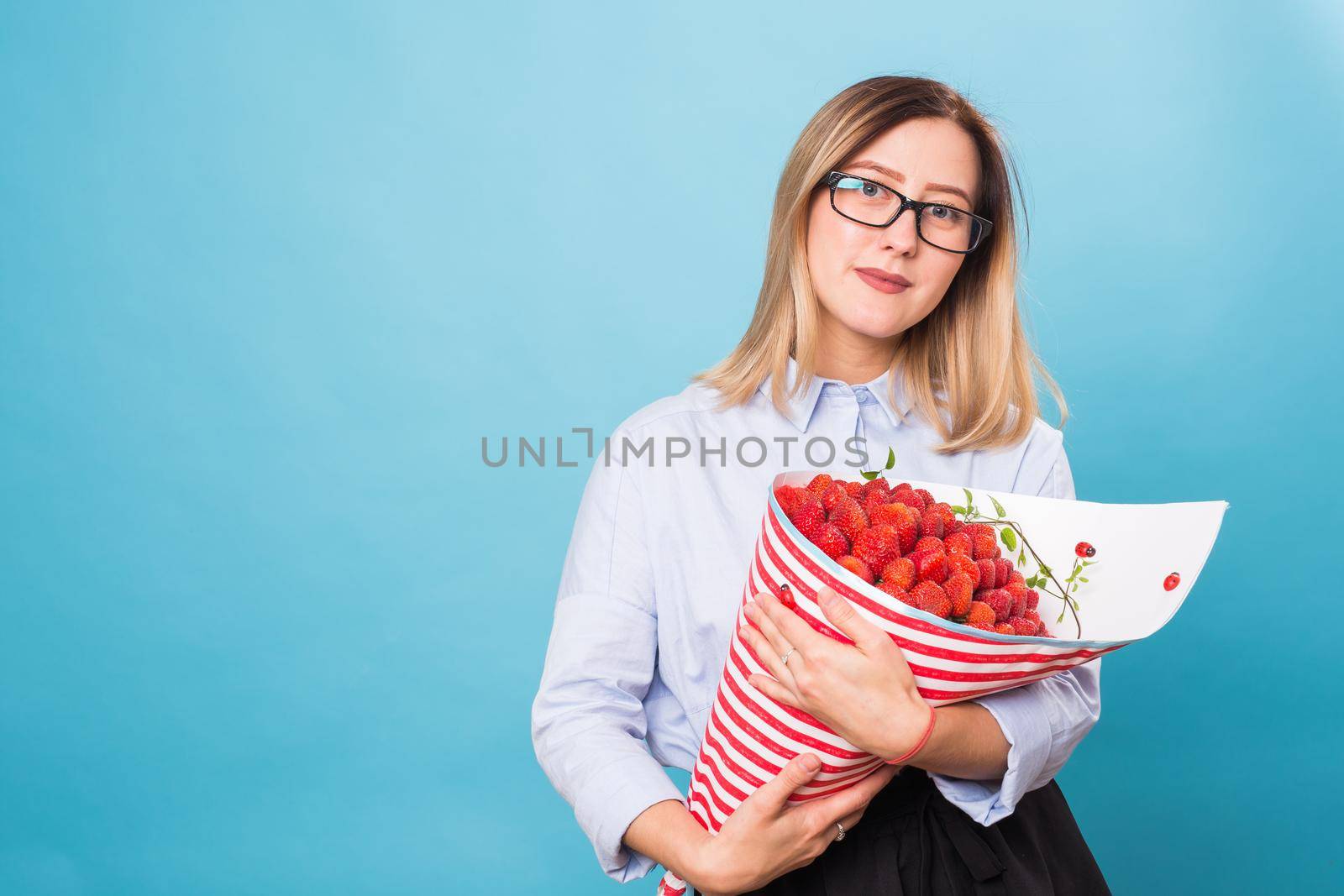 Young woman holding bouquet of strawberries on blue background. by Satura86