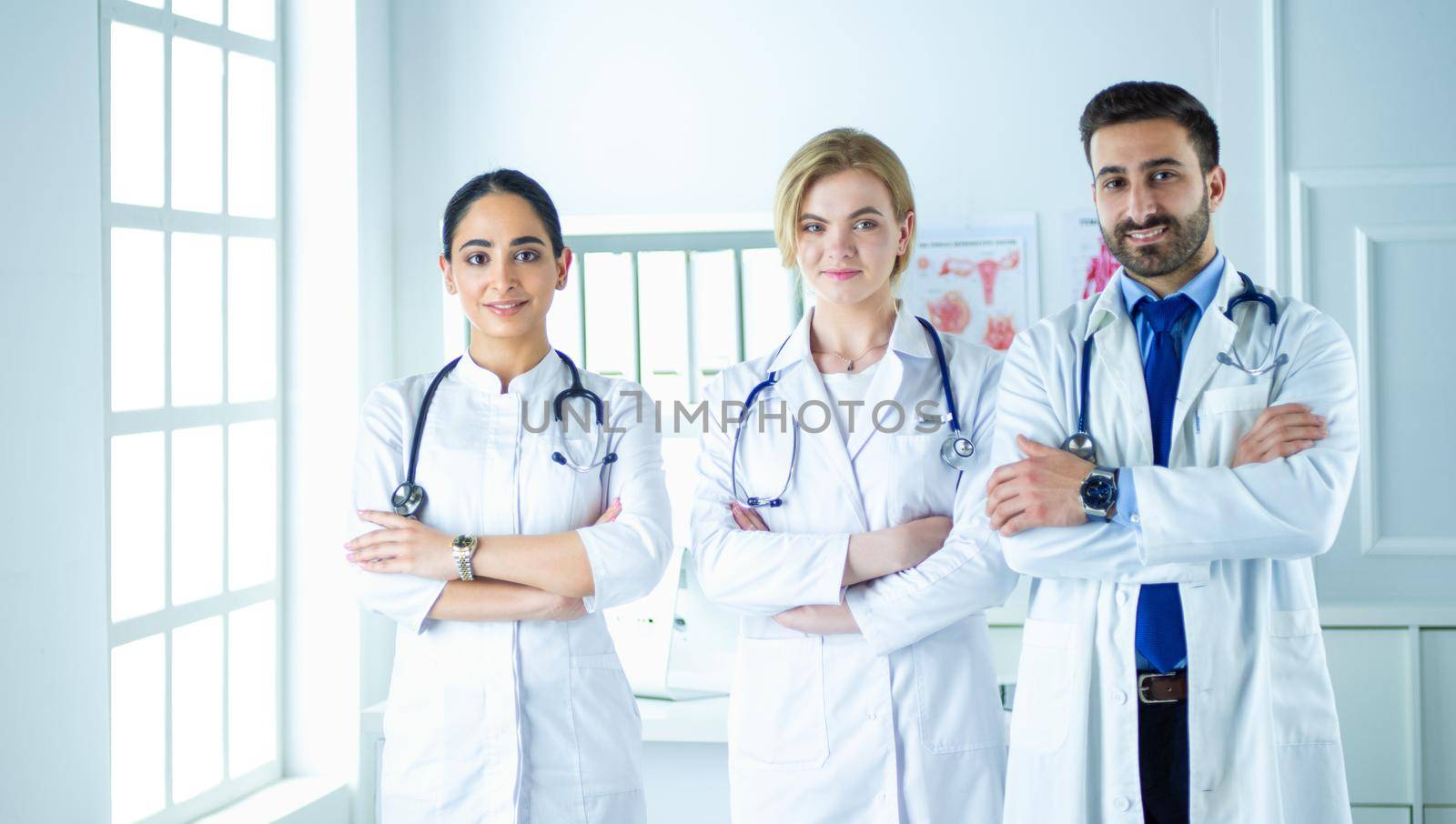 Successful team of medical doctors are looking at camera and smiling while standing in hospital.