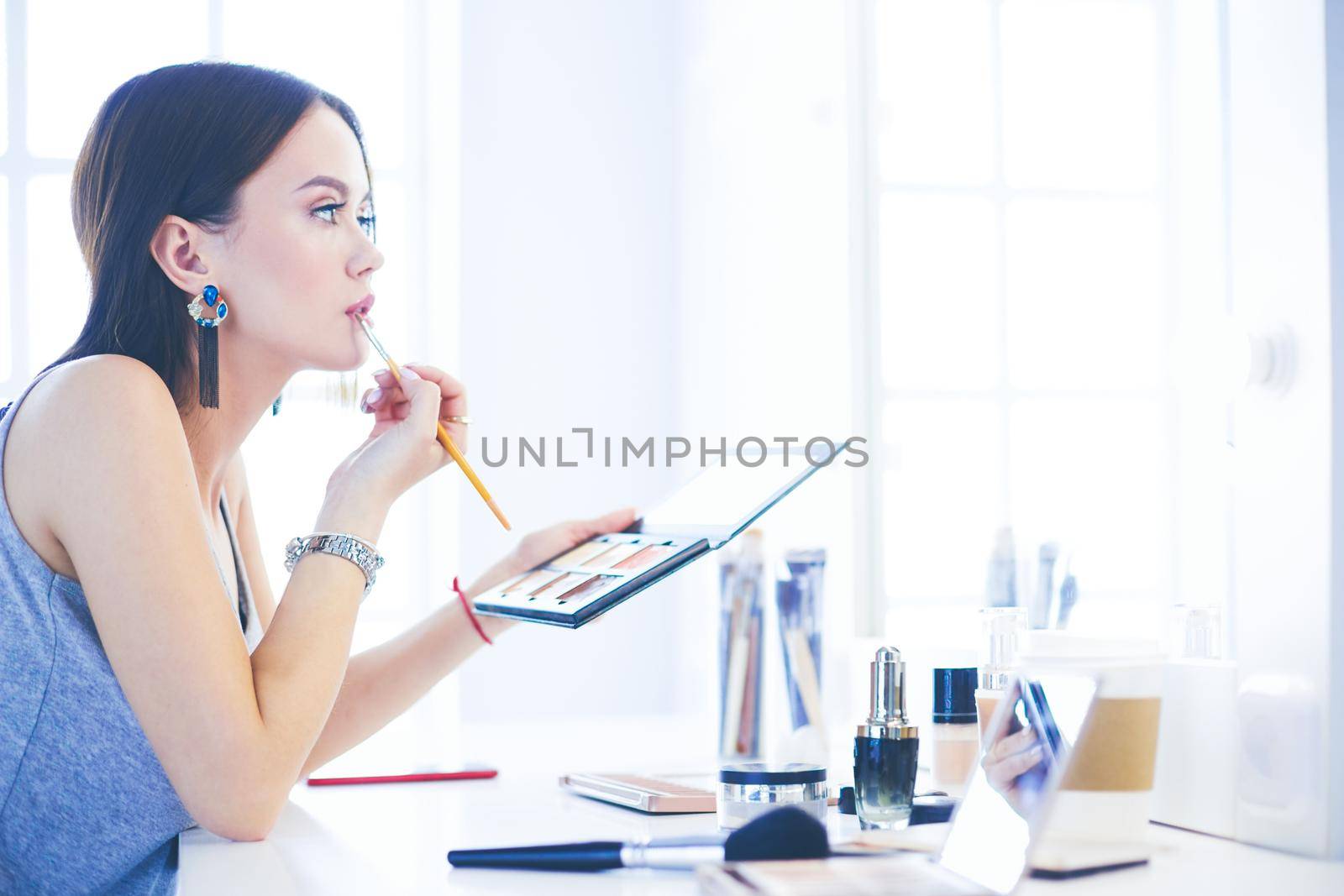 Brunette woman applying make up for a evening date in front of a mirror.