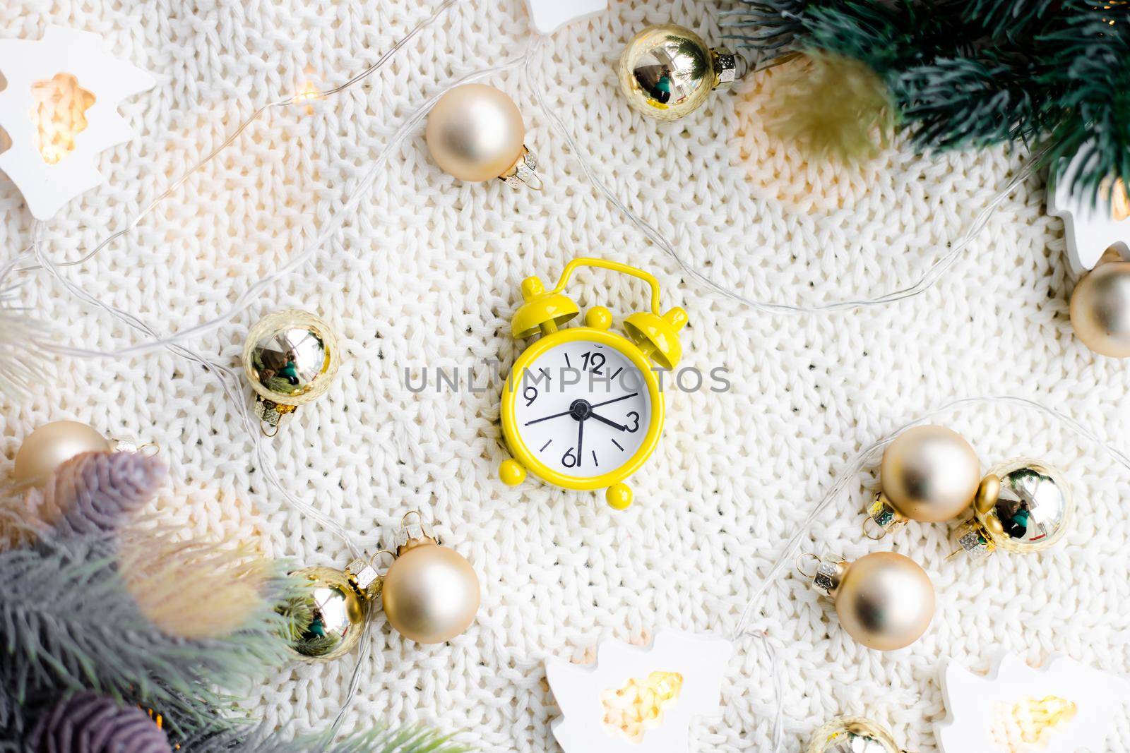 Alarm clock on a plaid with a garland . Yellow alarm clock. Cozy vibes . Home comfort. New Year and Christmas. Decorating