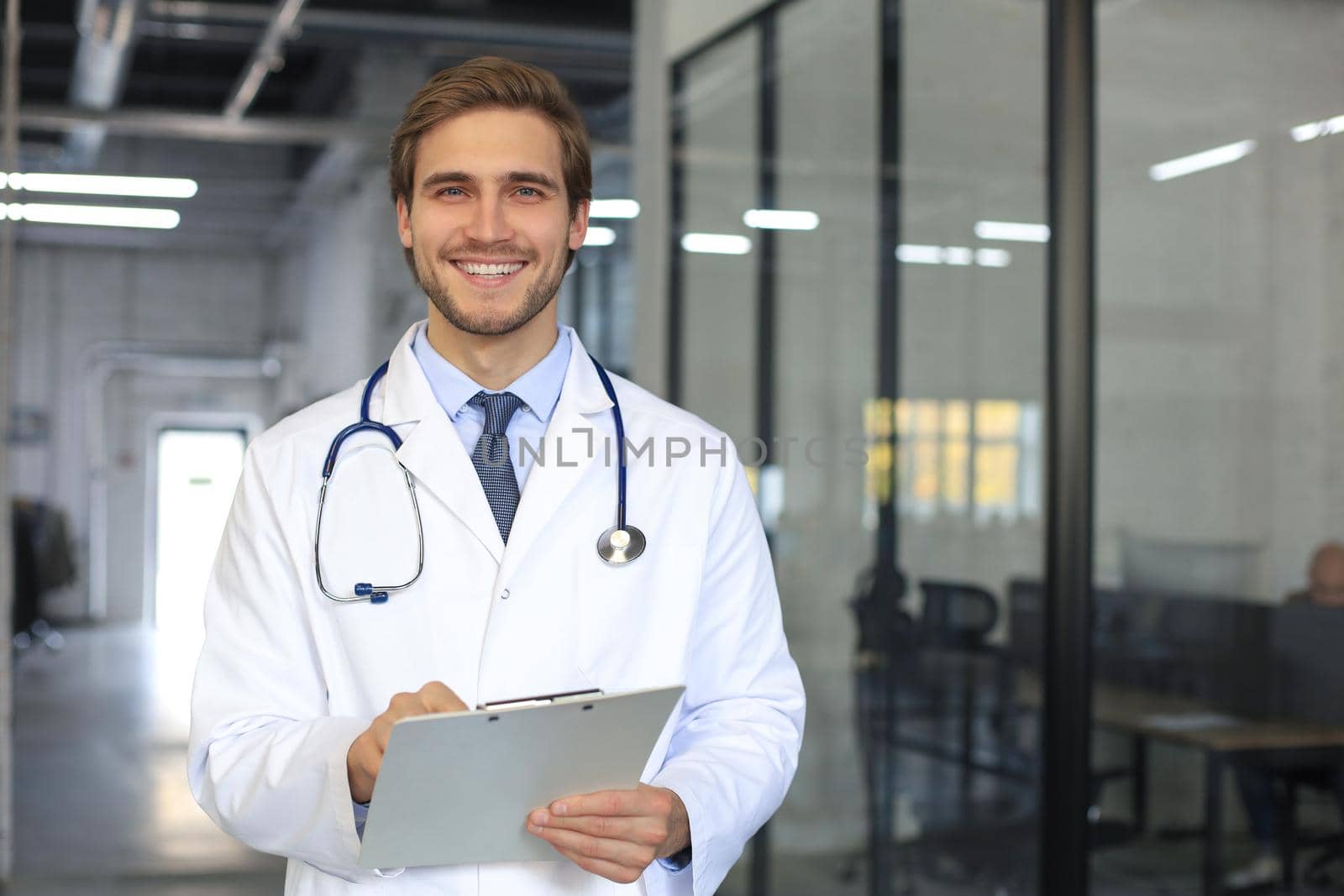 Handsome friendly young doctor on hospital corridor looking at camera, smiling