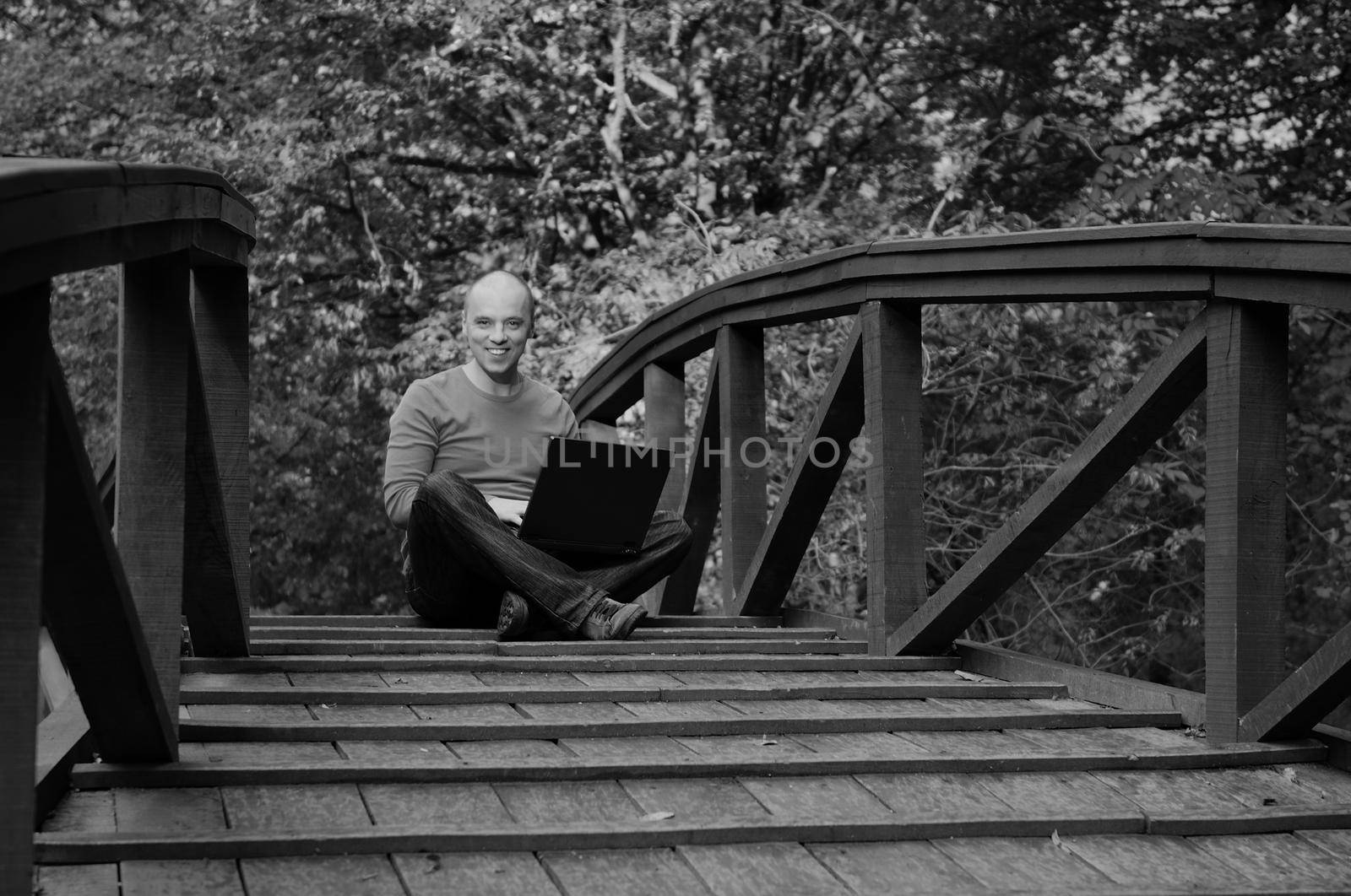 one young businessman working on laptop outdoor at wooden bridge  with green nature in background