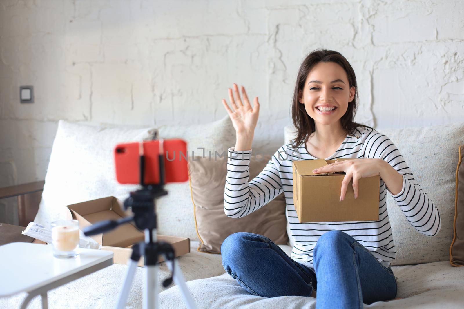 Young beautiful female blogger recording video while unpacking parcel at home