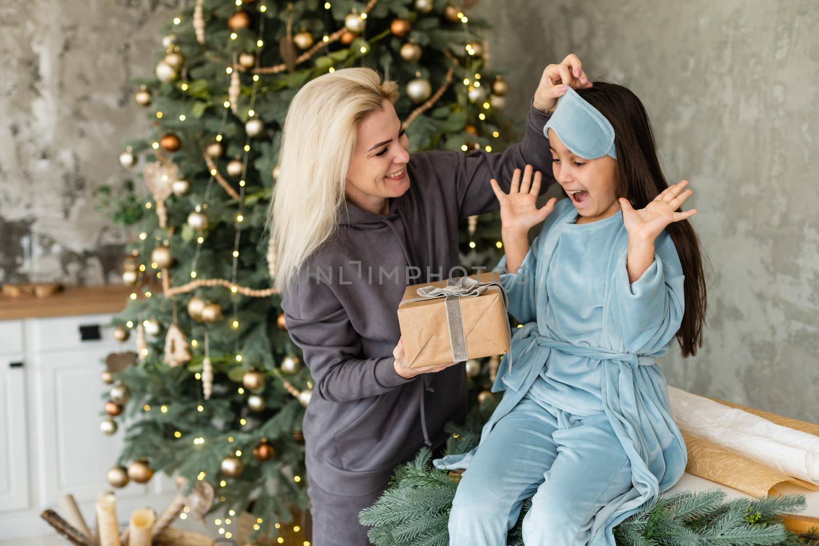 Merry Christmas and Happy Holidays, Cheerful mom and her cute daughter girl exchanging gifts. Parent and little child having fun near Christmas tree indoors. Loving family with presents in room.