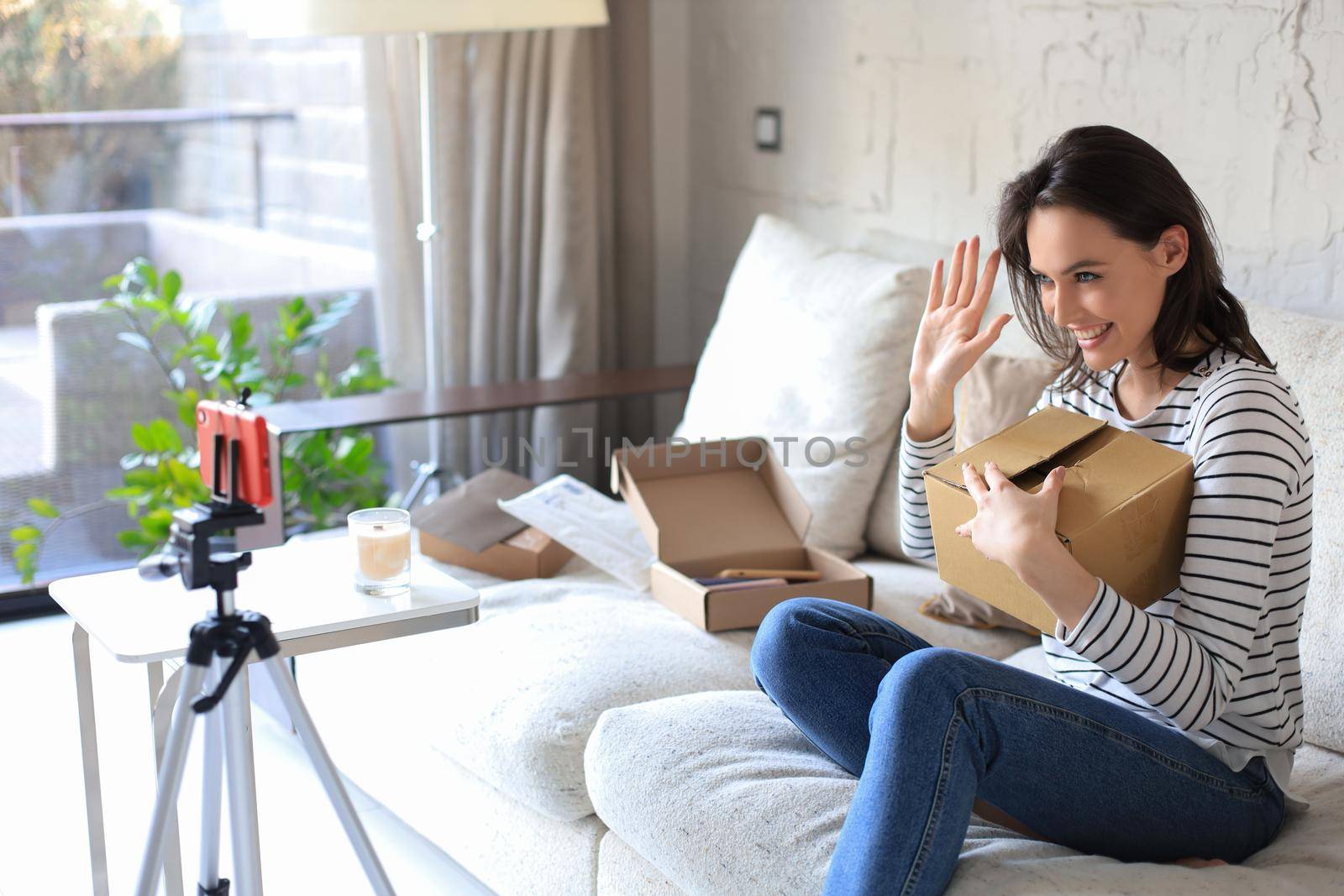 Young beautiful female blogger recording video while unpacking parcel at home
