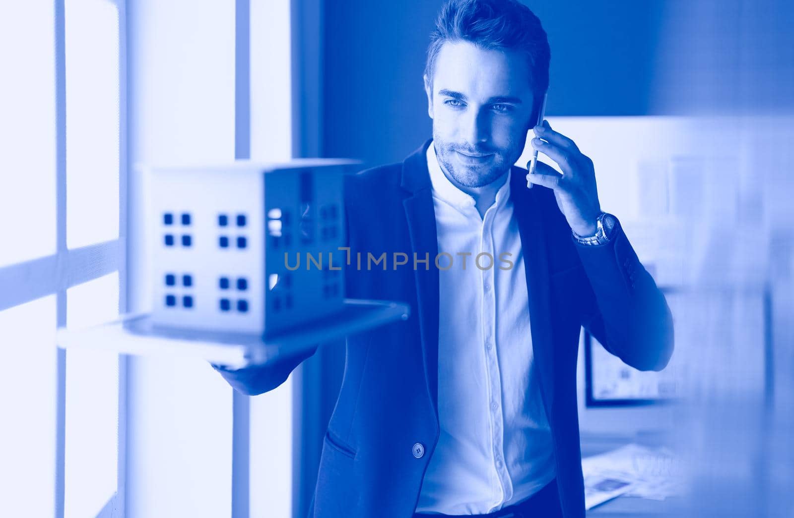 Businessman holding house miniature on hand standing in office