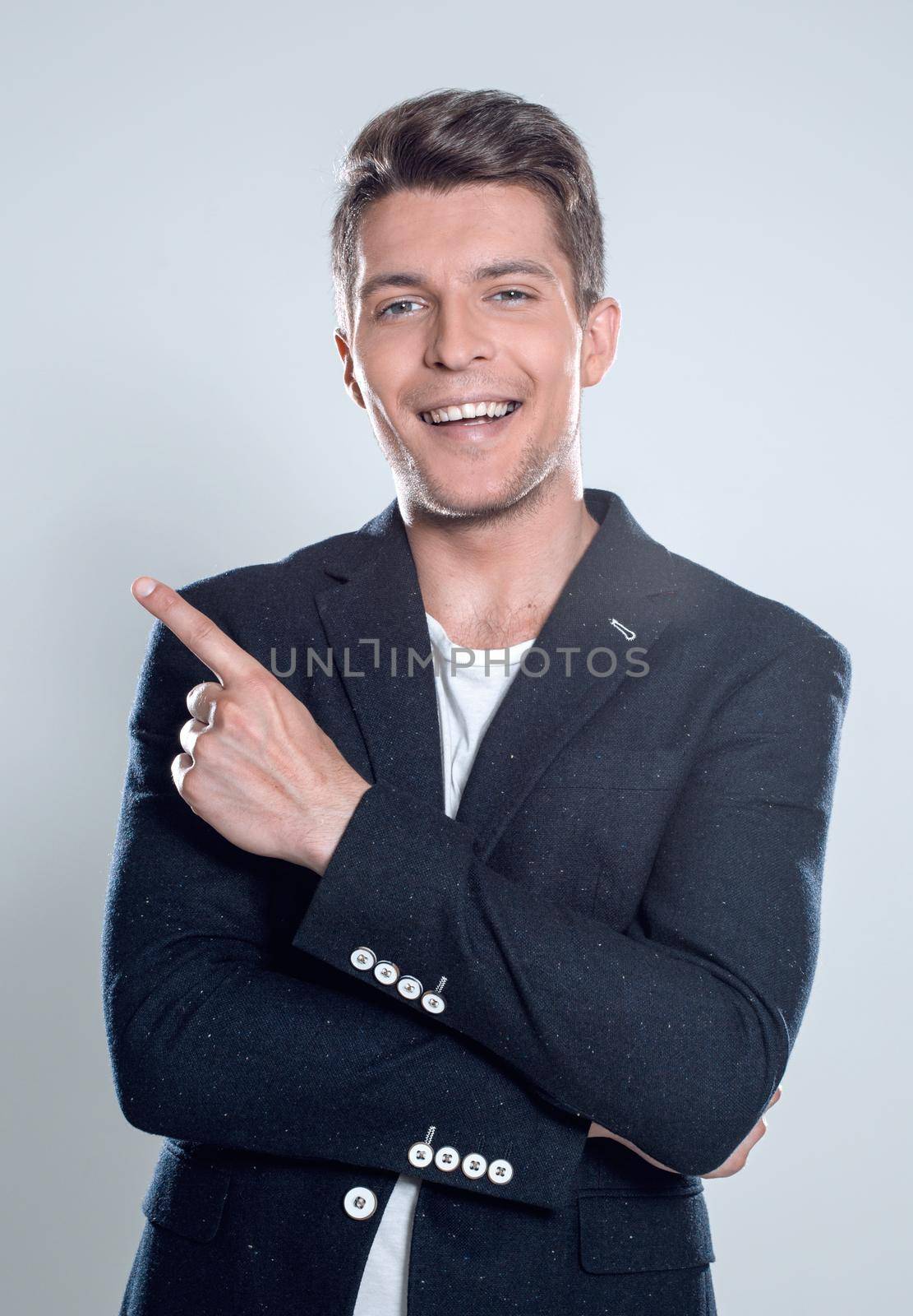 Close up portrait of young successful brunete stock-market broker guy on the gray background, he is smiling and is pointing on a copyspace with his finger