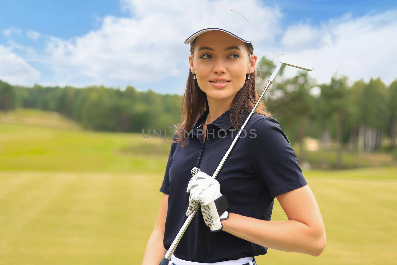 Professional female golfer holding golf club on field and looking away. Young woman standing on golf course on a sunny day.