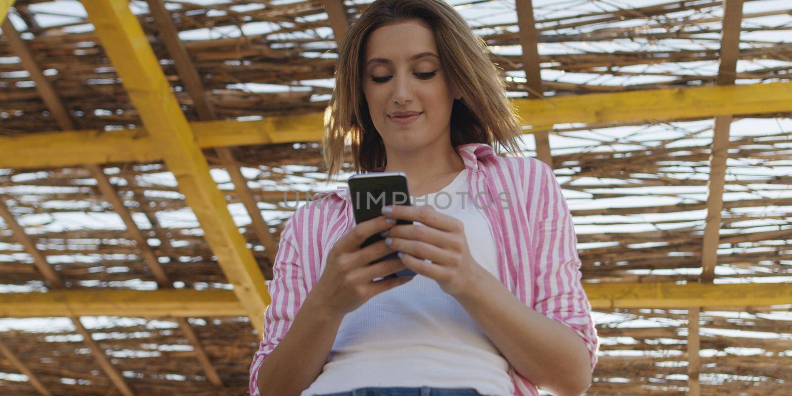 young woman using mobile cell smart phone app at beach during sunset on autumn day