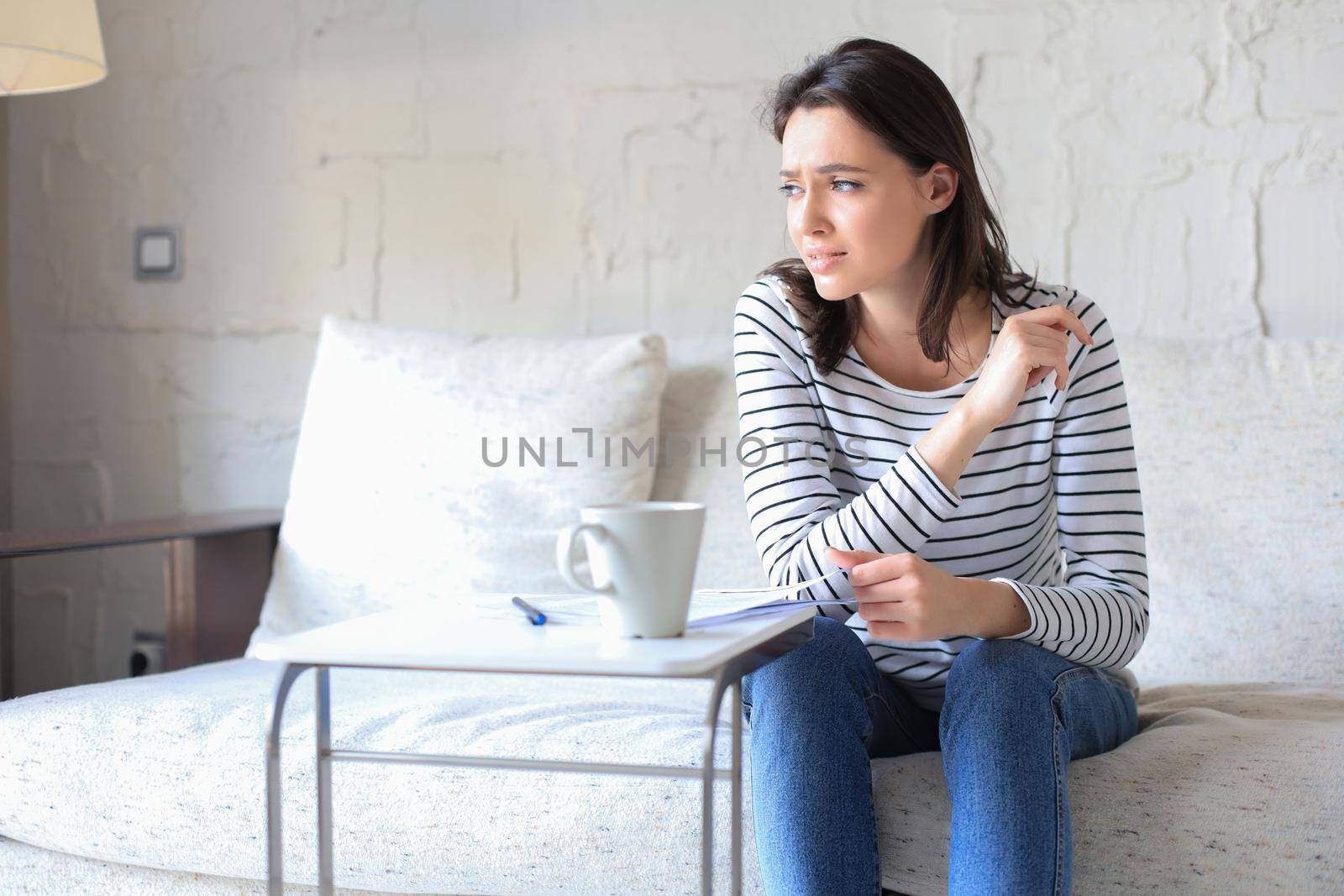 Sad woman with the bills sitting on a sofa in the living room