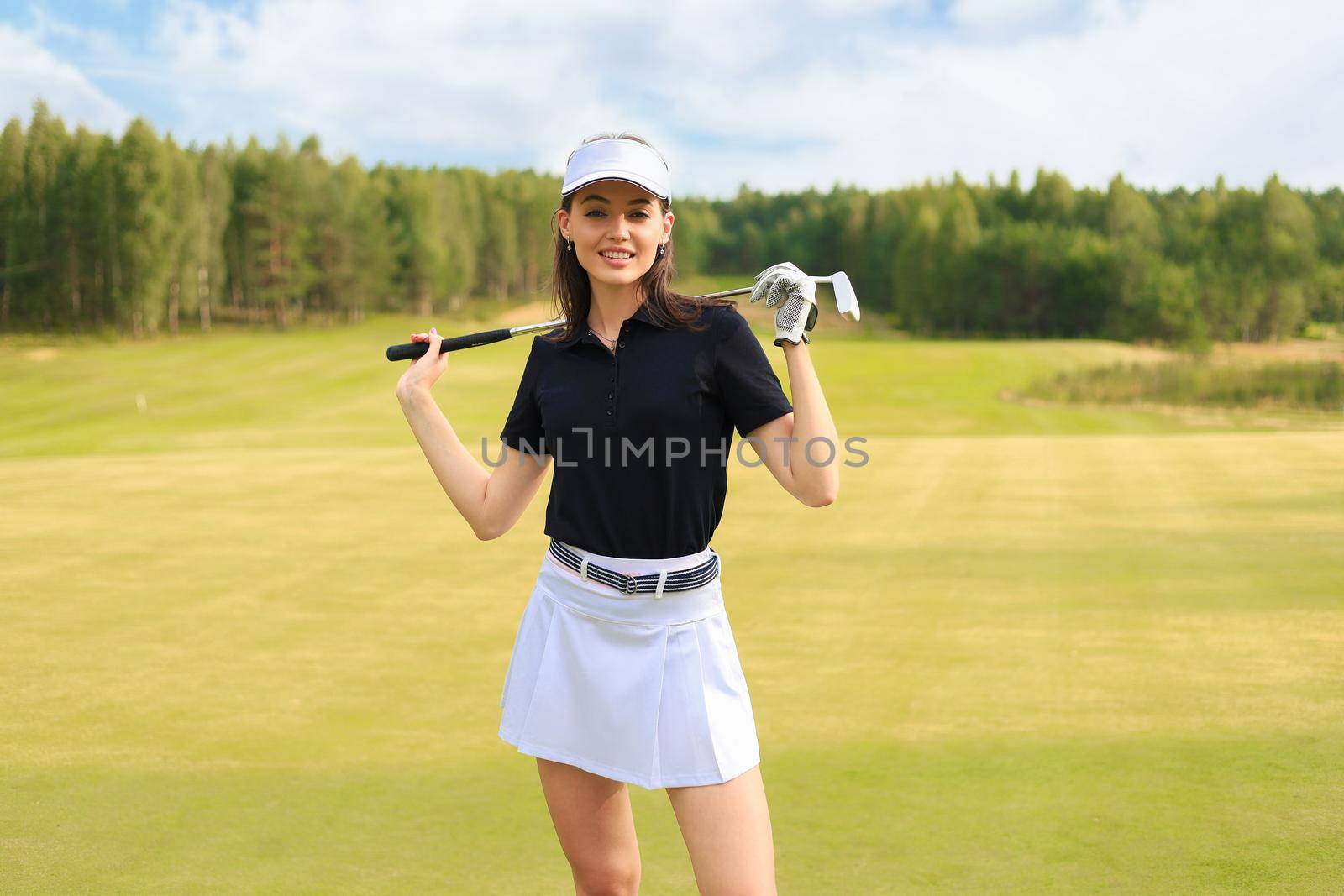 Professional female golfer holding golf club on field and looking away. Young woman standing on golf course on a sunny day.