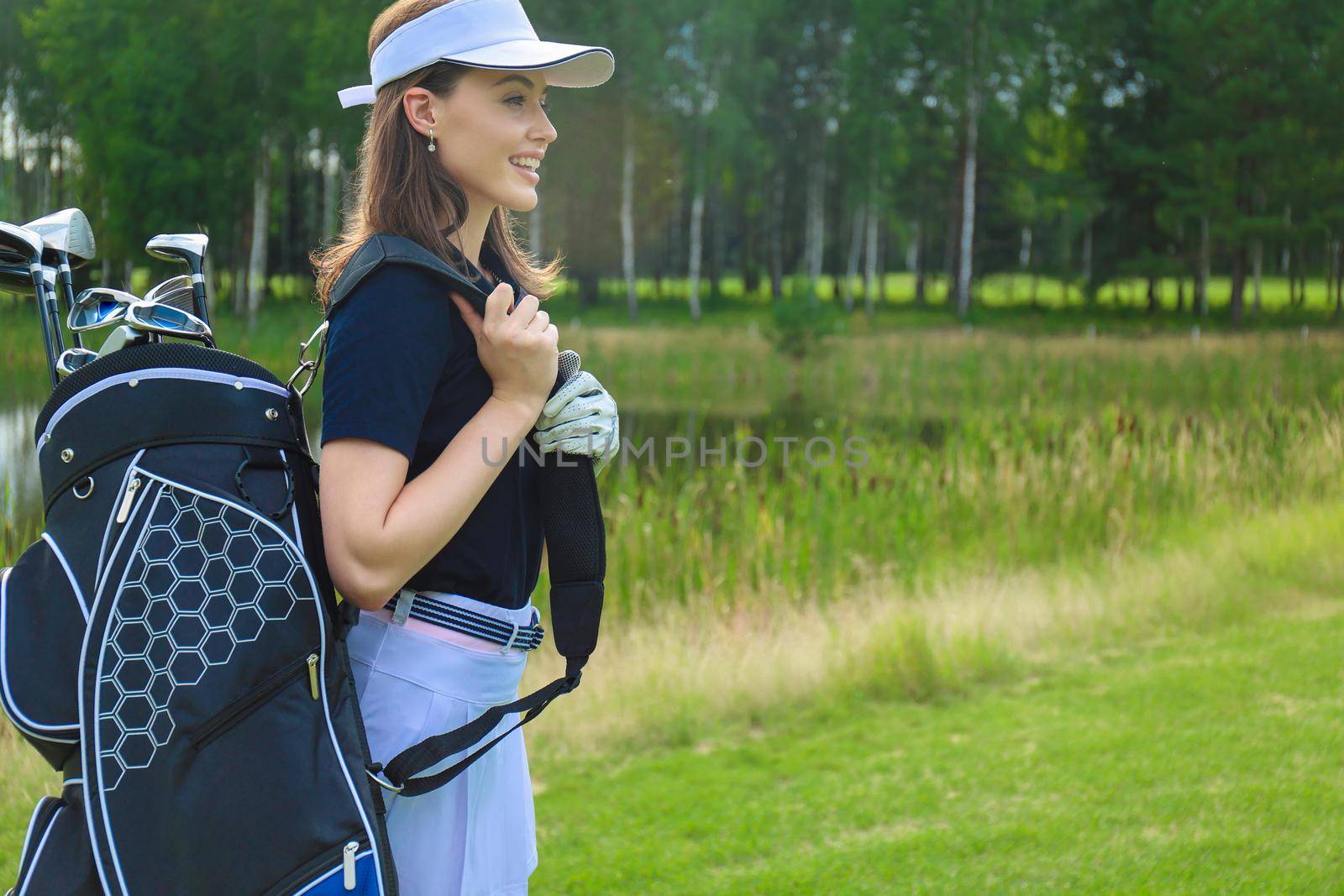 Beautiful golf woman player carrying a golf bag and smiling
