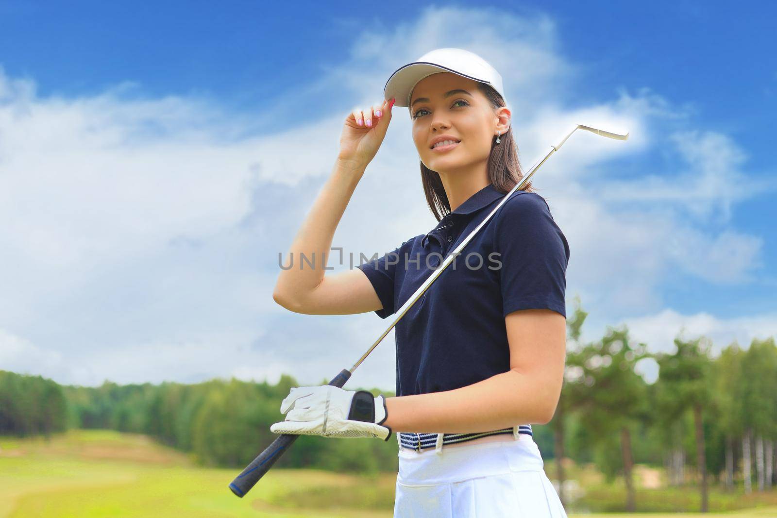 Professional female golfer holding golf club on field and looking away. Young woman standing on golf course on a sunny day.