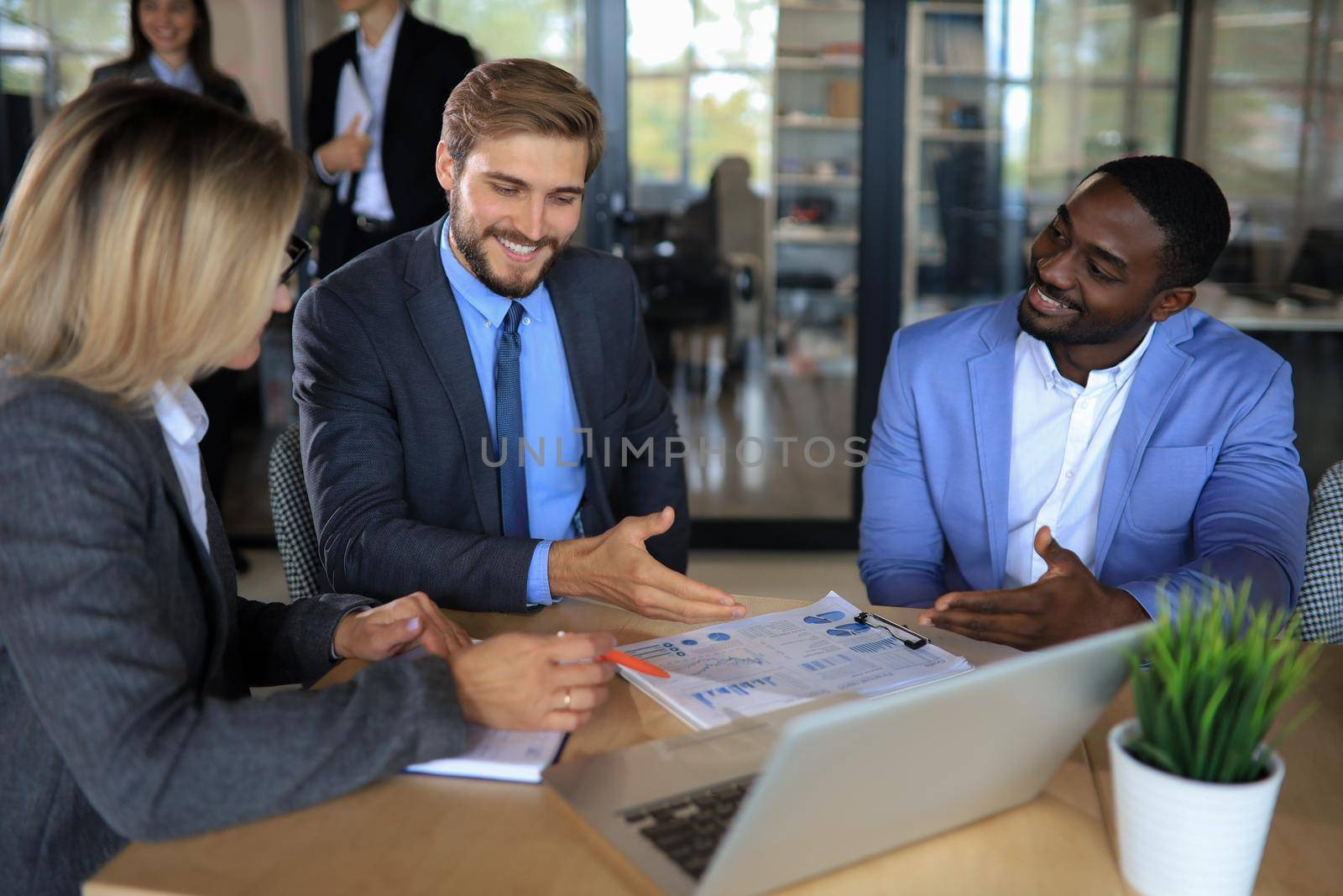 Group of happy diverse male and female business people in formal gathered around laptop computer in bright office