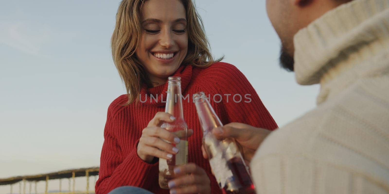 Young Couple Relaxing By The Fire, Drinking A Beer Or A Drink From The Bottle.